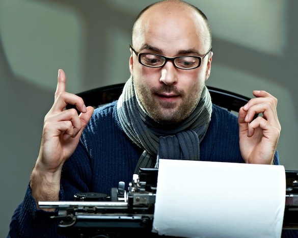 Old fashioned bald writer in glasses writing book on a vintage typewriter